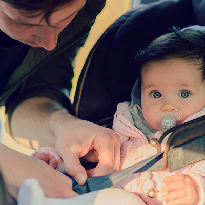 Baby being buckled into a car sheet by dad