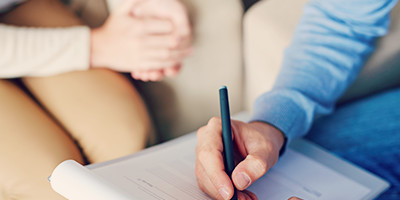 man and woman in a counseling session taking notes. Man is holding a pen over a form