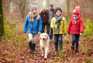 family walking through the woods during fall with winter jackets on and a dog
